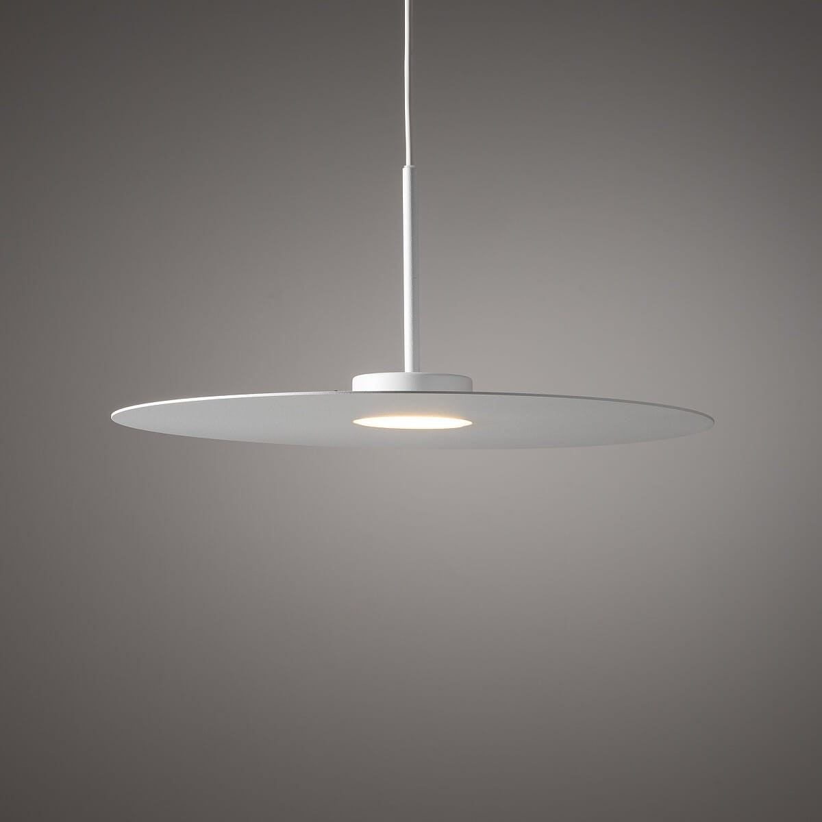 Biała lampa wisząca Simone z pojedynczym źródłem światła GX53, o okrągłej, płaskiej konstrukcji. Zawieszona na cienkim kablu, widoczna w neutralnym tle, idealna do nowoczesnych wnętrz.