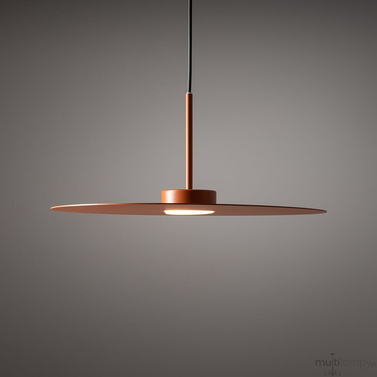 Lampa wisząca Simone w kolorze ceglanym z metalowym kloszem o okrągłym kształcie. Zamontowana na cienkim przewodzie, z centralnym źródłem światła wbudowanym w okrągłą podstawę. Ujęcie frontalne, na jednolitym tle.