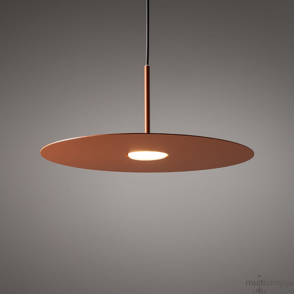 Lampa wisząca Simone w kolorze ceglastym, z okrągłym, płaskim kloszem i centralnym źródłem światła. Zawieszona na cienkim, czarnym przewodzie. Prosta, nowoczesna forma, idealna do wnętrz minimalistycznych.