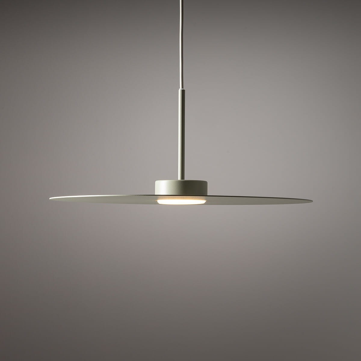 Lampa wisząca Simone w kolorze szałwii, z jednym źródłem światła GX53. Posiada okrągły, płaski klosz oraz długi, smukły przewód. Ujęcie frontalne, na szarym tle.