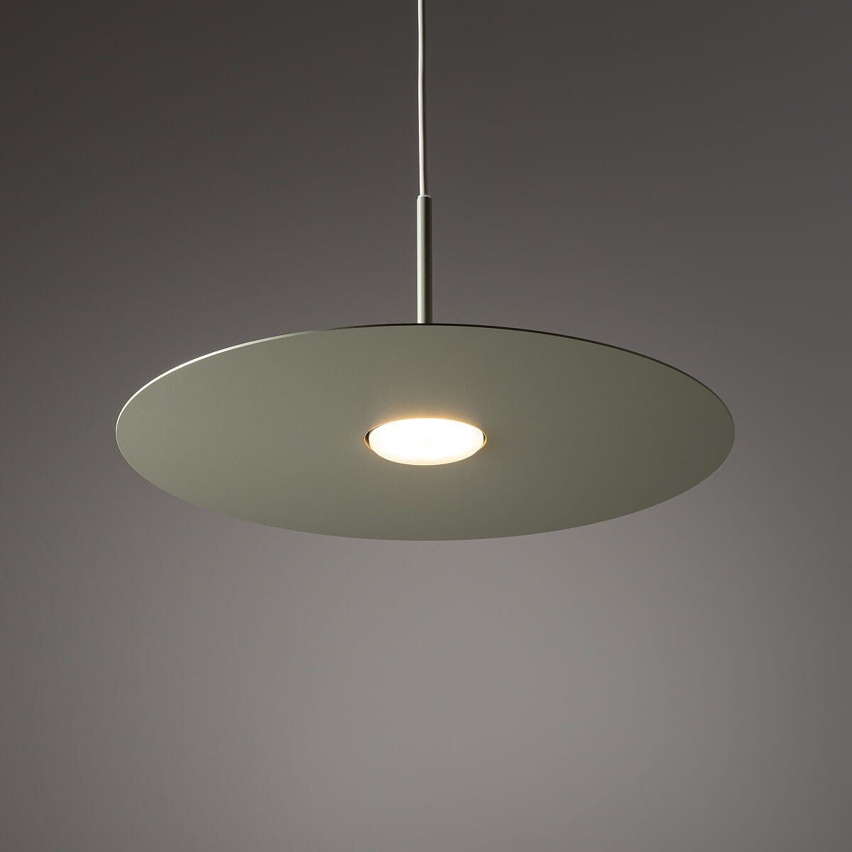Lampa wisząca Simone w kolorze szałwii z okrągłym kloszem. Zawieszona na cienkim metalowym uchwycie, z centralnym źródłem światła GX53. Klosz ma matową, gładką powierzchnię, co nadaje elegancki wygląd. Tło jest jednolite, ciemnoszare.