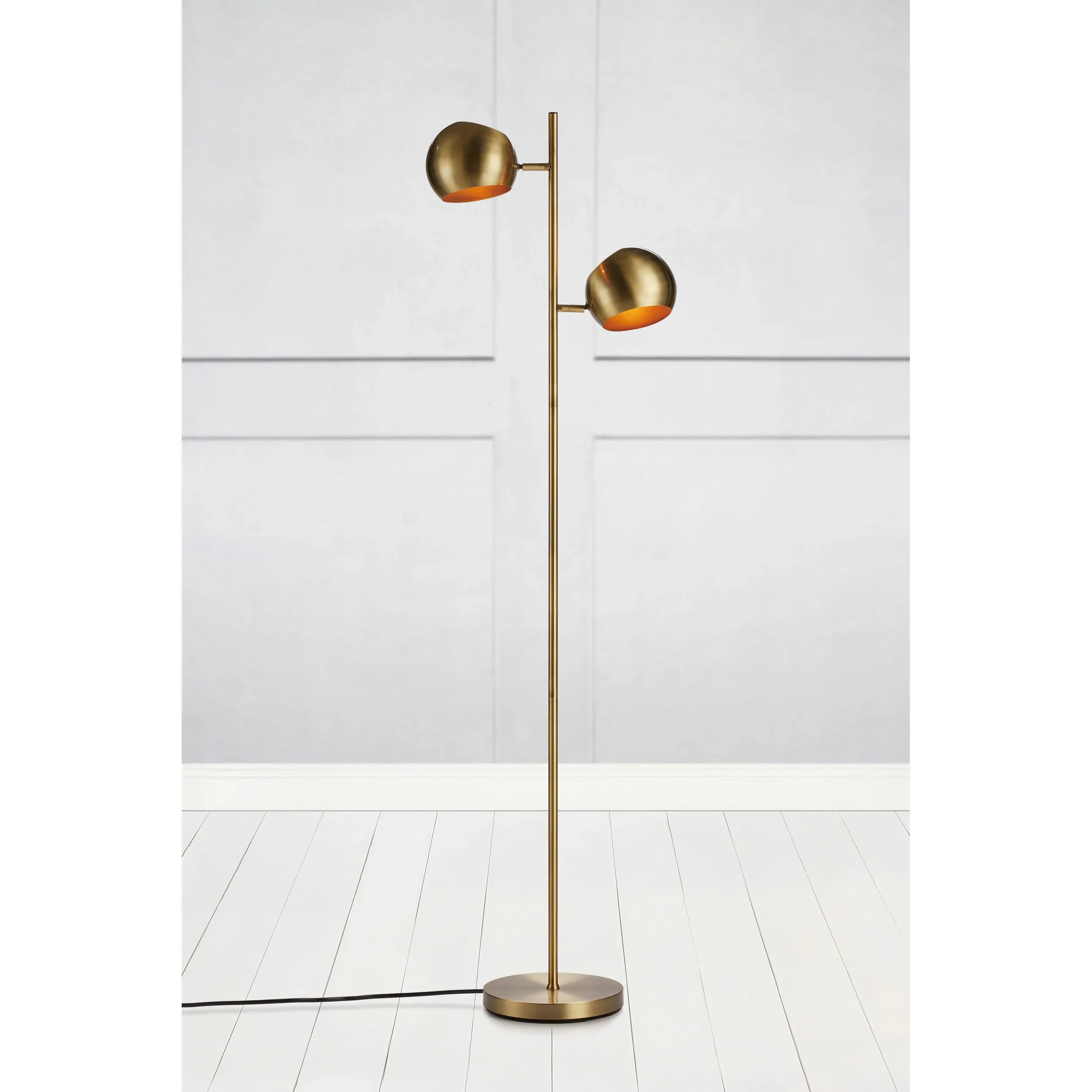 Lampa podłogowa Edgar w kolorze patynowym, z dwoma reflektorami o okrągłym kształcie. Stojąca na okrągłej podstawie, z cienką, prostą nogą. Reflektory skierowane w górę, z wewnętrzną pomarańczową powłoką. Tło jasne, minimalistyczne.