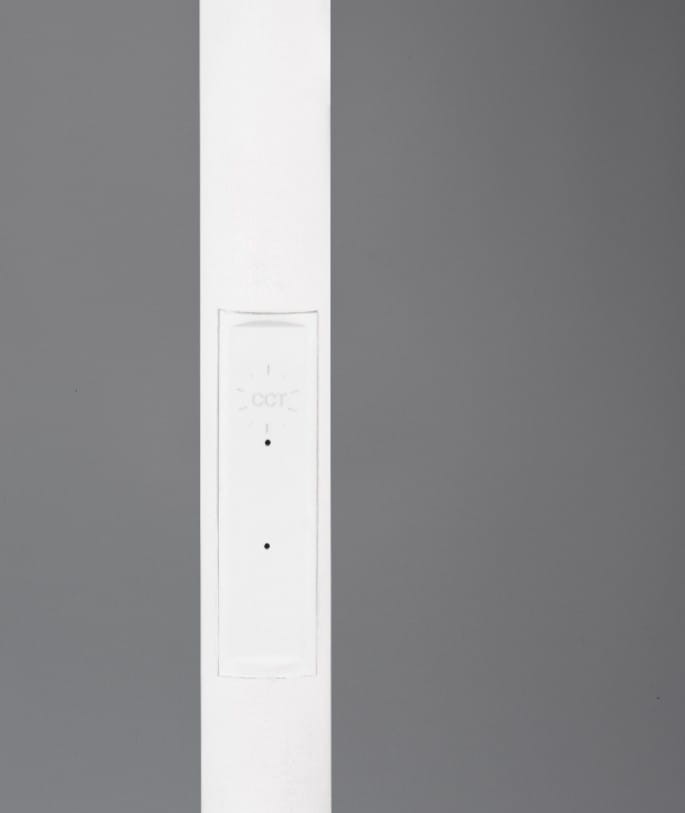 Biała lampa podłogowa Specter z jednym źródłem LED o mocy 17W. Zbliżenie na prostą, smukłą konstrukcję z widocznym panelem sterującym. Tło w odcieniu szarości.