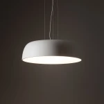 Lampa wisząca Satellite M w kolorze białym, o okrągłej, płaskiej formie, z miejscem na 7 żarówek E27. Zawieszona na cienkich linkach, emitująca jasne światło, umieszczona na ciemnym tle.