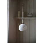 Lampa wisząca Lohals w kolorze białym z metalowym elementem, o okrągłym kształcie z wyciętymi wzorami. Zawieszona na cienkim przewodzie, z widocznym detalem w postaci dekoracyjnych otworów, wisi na tle jasnej ściany.