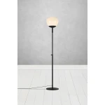 Lampa podłogowa Rise 1-punktowa w kolorze czarnym z białym kloszem, stojąca na okrągłej, czarnej podstawie. Ujęcie frontalne, w tle szare ściany i biała podłoga. Kabel zasilający widoczny obok nogi lampy.