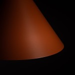 Lampa wisząca Zenith M w kolorze ceglastym, z metalowym kloszem o stożkowym kształcie. Ujęcie zbliżeniowe na górną część klosza, ukazujące gładką, matową fakturę. Tło ciemne, podkreślające intensywność koloru.