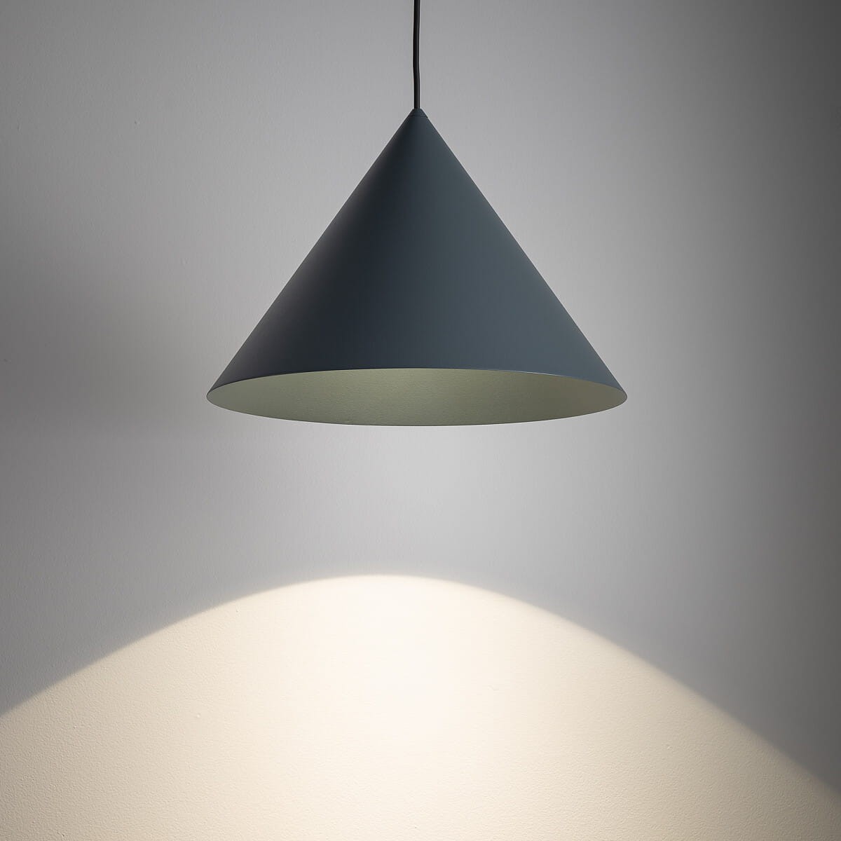 Niebieska lampa wisząca Zenith M o kształcie stożka, zwisająca na czarnym przewodzie. Wnętrze klosza jasne, emitujące światło na ścianę. Idealna do nowoczesnych wnętrz. Widok frontalny.