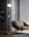 Lampa podłogowa Chris z dwoma źródłami LED, czarna z kawowymi akcentami. Okrągłe klosze w górnej i dolnej części na smukłych ramionach. Stojąca na okrągłej podstawie, obok wygodnego fotela w stonowanej aranżacji.