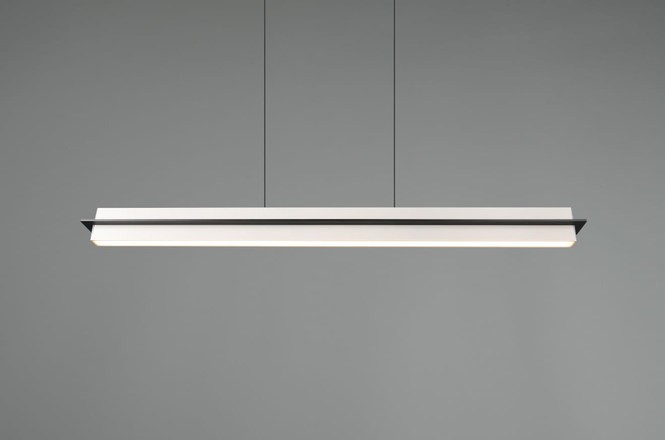 Lampa wisząca Emerson w kolorze szarym, o prostej, wydłużonej formie. Wyposażona w jedno źródło światła LED o mocy 22W. Zawieszona na cienkich linkach, z białą oprawą i czarnymi akcentami, na jednolitym tle.