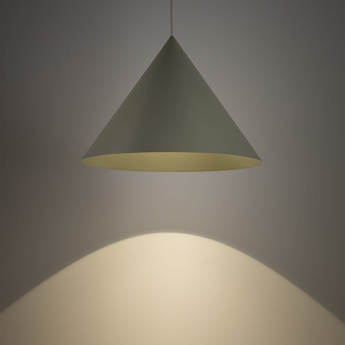 Lampa wisząca Zenith L w kolorze szałwii, w kształcie stożka, zawieszona na cienkim przewodzie. Emituje ciepłe światło, które tworzy delikatny cień na ścianie. Wykończenie matowe, minimalistyczny design, idealna do nowoczesnych wnętrz.