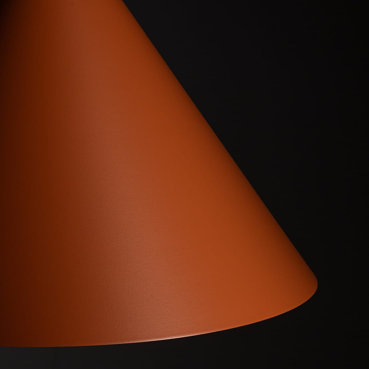 Lampa wisząca Zenith L w kolorze ceglastym z kloszem w kształcie stożka, wykonana z matowego materiału. Ujęcie z boku, pokazujące detale wykończenia. Przeznaczona do jednego źródła światła typu GU10. Tło ciemne, co podkreśla kolor lampy.