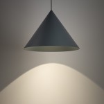 Lampa wisząca Zenith L w kolorze niebieskim, o kształcie stożka, zawieszona na cienkim przewodzie. Emituje światło skierowane w dół, tworząc delikatny cień na ścianie. Pasuje do nowoczesnych wnętrz. Wymaga żarówki GU10.