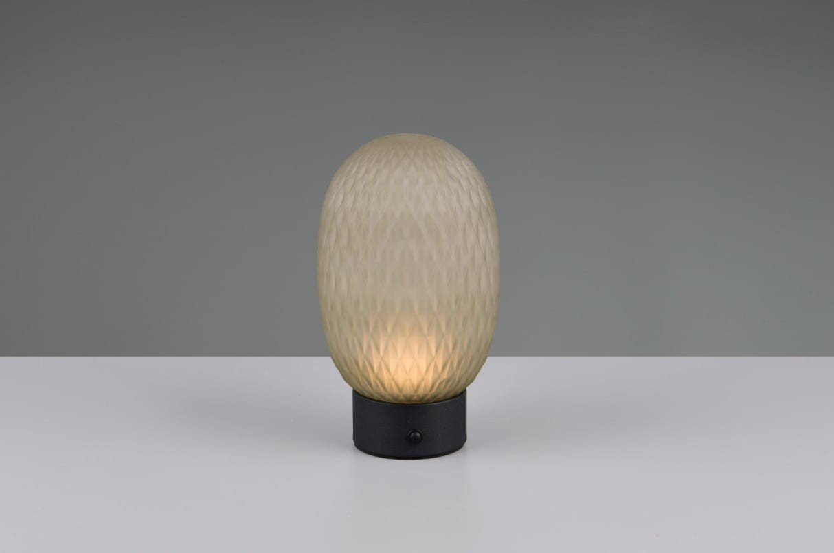 Lampa stołowa Facette w kolorze czarnym i zielonym z podstawką z metalu. Owalny klosz z teksturowanego szkła w ciepłym odcieniu, emitujący światło LED o mocy 1,5W. Ujęcie frontalne na białym tle, lampa stoi na równym podłożu.