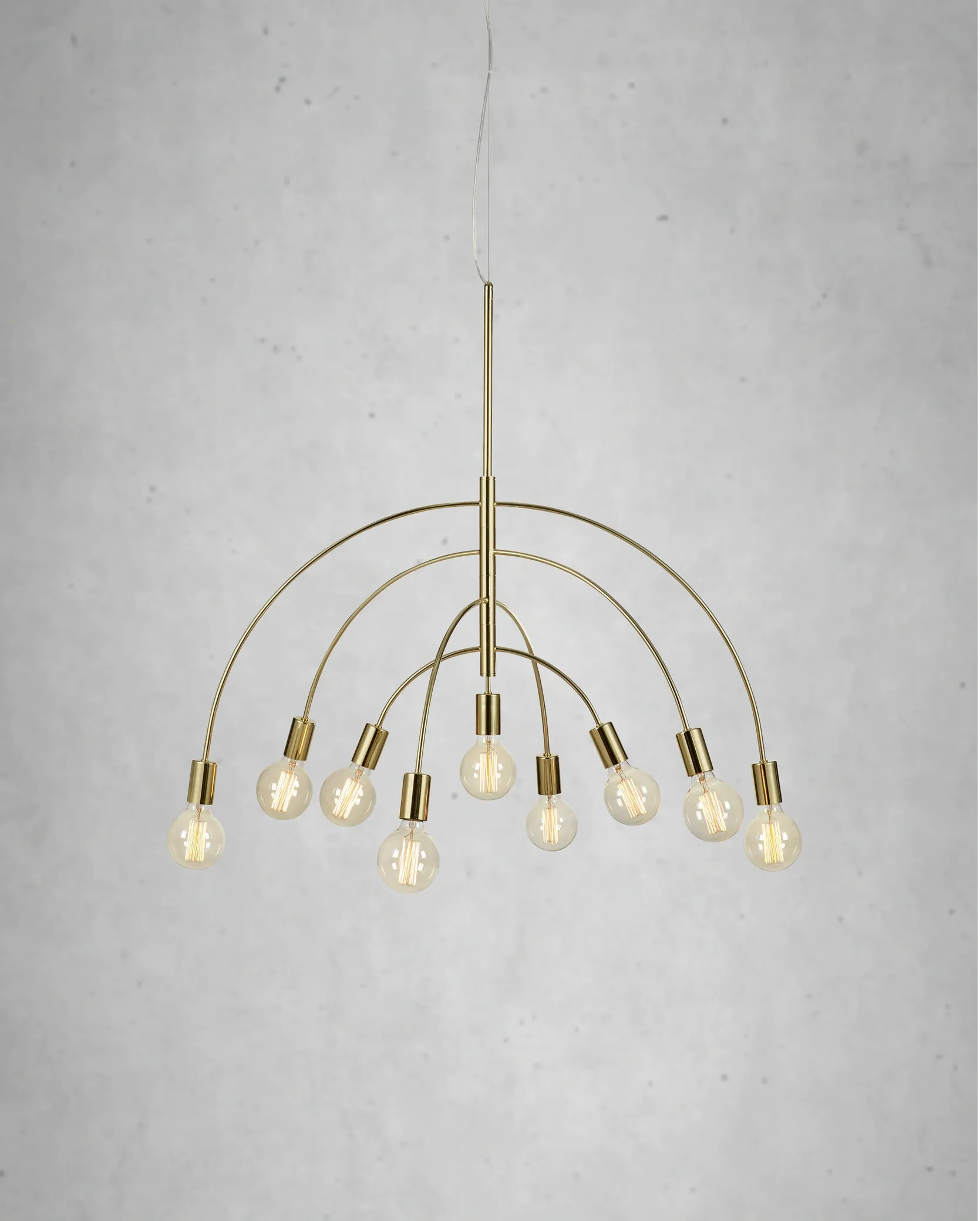 Lampa wisząca Lavello 9-punktowa w kolorze mosiądzu, z eleganckimi, zaokrąglonymi ramionami. Wyposażona w dziewięć żarówek, zawieszona na cienkim kablu. Tło w odcieniach szarości, podkreślające stylowy design.