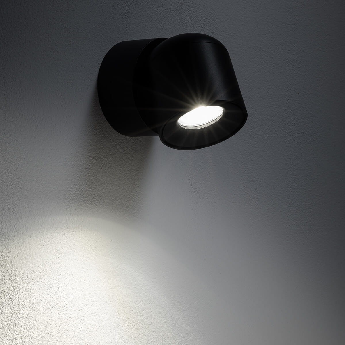 Czarna lampa sufitowa Oscar z pojedynczym spotem GU10, montowana na ścianie. Kąt ujęcia z boku, ukazujący źródło światła i jego efekt na ścianie. Wodoodporna konstrukcja IP54, minimalistyczny design, idealna do wnętrz i na zewnątrz.