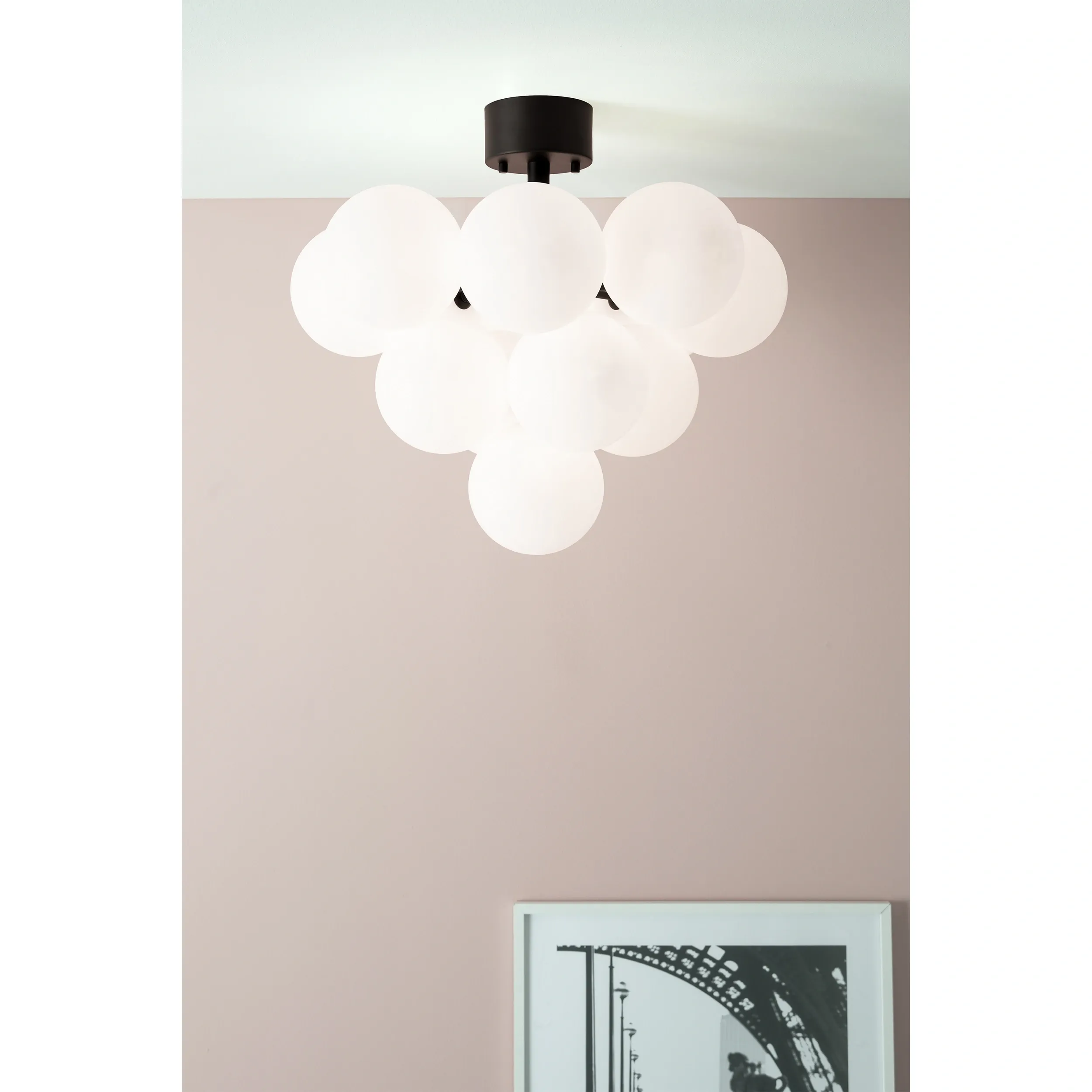 Lampa sufitowa Merlot, 13-punktowa, w kolorze czarnym i białym. Składa się z dużych, matowych kul, zawieszonych na czarnej podstawie. Ujęcie z dołu, na tle różowej ściany, z widocznym fragmentem ramki ze zdjęciem poniżej.