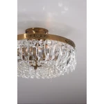 Lampa sufitowa Stromsholm 3-punktowa w stylu antycznym, z metalowym, złotym wykończeniem. Zdobiona kryształowymi wiszącymi elementami, tworzy efektowną iluminację. Ujęcie z dołu, z widocznymi detalami kryształów i dekoracyjnym obręczem.
