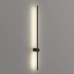Kinkiet Catrina 90 w kolorze czarnym, zamontowany na ścianie. Składa się z pionowego, cienkiego ramienia z wbudowanym źródłem światła LED o mocy 14W i temperaturze barwowej 4000K, emitującym ciepłe światło. Tło jasnoszare.