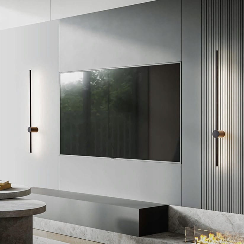 Kinkiet Catrina 90 w kolorze czarnym, z jedną diodą LED o mocy 14W i temperaturze barwowej 4000K. Montowany na ścianie obok telewizora, z minimalistycznym designem i cylindrycznym uchwytem. Widoczny w nowoczesnym wnętrzu.