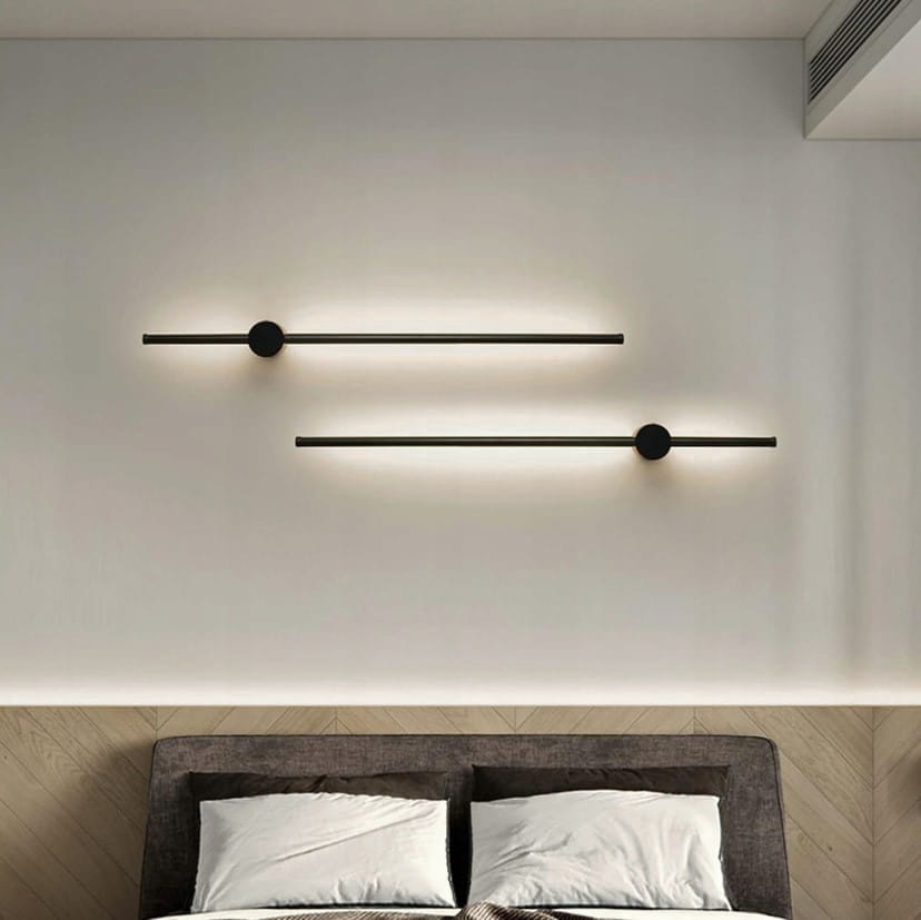 Catrina 90 kinkiet w kolorze czarnym, z jedną diodą LED o mocy 14W i temperaturze barwowej 4000K. Montowany na ścianie, minimalistyczny design z poziomą linią i okrągłym detalem. Widoczny na tle jasnej ściany nad łóżkiem.