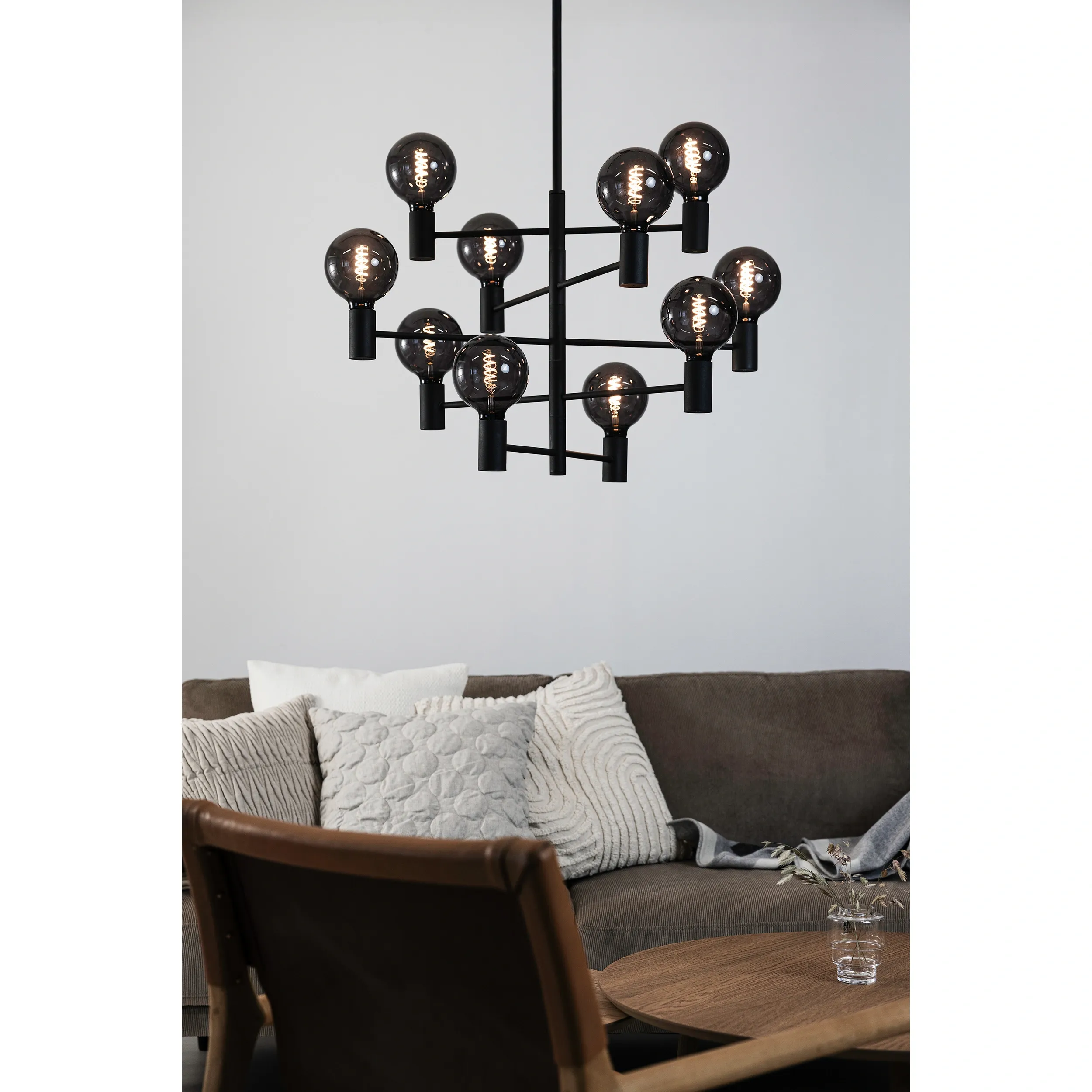Czarna lampa wisząca Paris z 10 punktami świetlnymi, o nowoczesnym designie. Widoczna w pomieszczeniu, zawieszona na długim przewodzie, z okrągłymi, przezroczystymi kloszami. Tło w jasnej tonacji, w aranżacji z sofą i poduszkami.