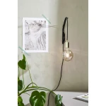 Lampa wisząca Sky 1-punktowa w kolorze złotym, z przezroczystą żarówką, zawieszona na czarnym kablu. Produkt umieszczony na tle szarej ściany, obok plakatu i zielonej rośliny. Kąt ujęcia z boku, ukazujący detale lampy.