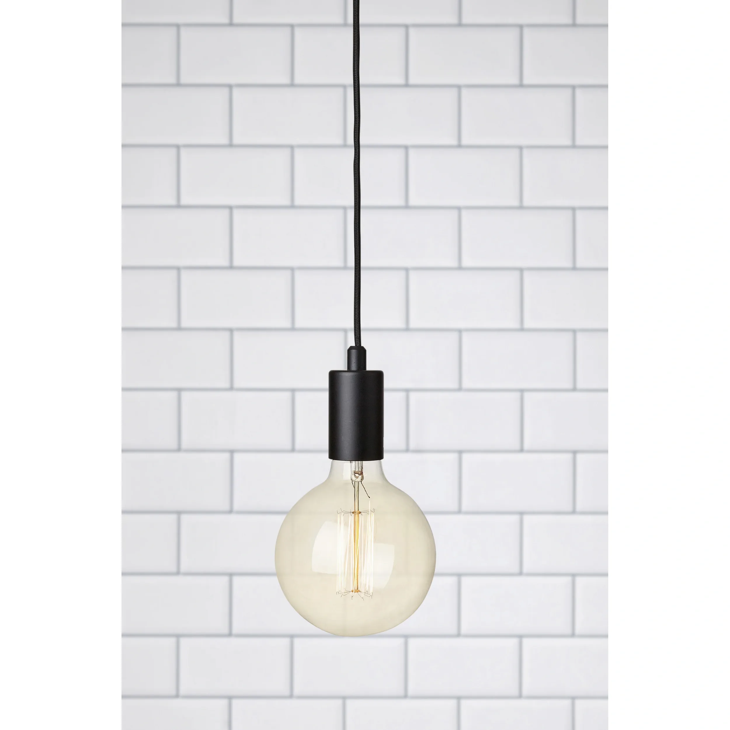 Czarna lampa wisząca Sky z pojedynczym punktem świetlnym. Okrągła, przezroczysta żarówka z widocznymi włóknami, zawieszona na długim czarnym kablu. Tło w jasnym, kafelkowym układzie.