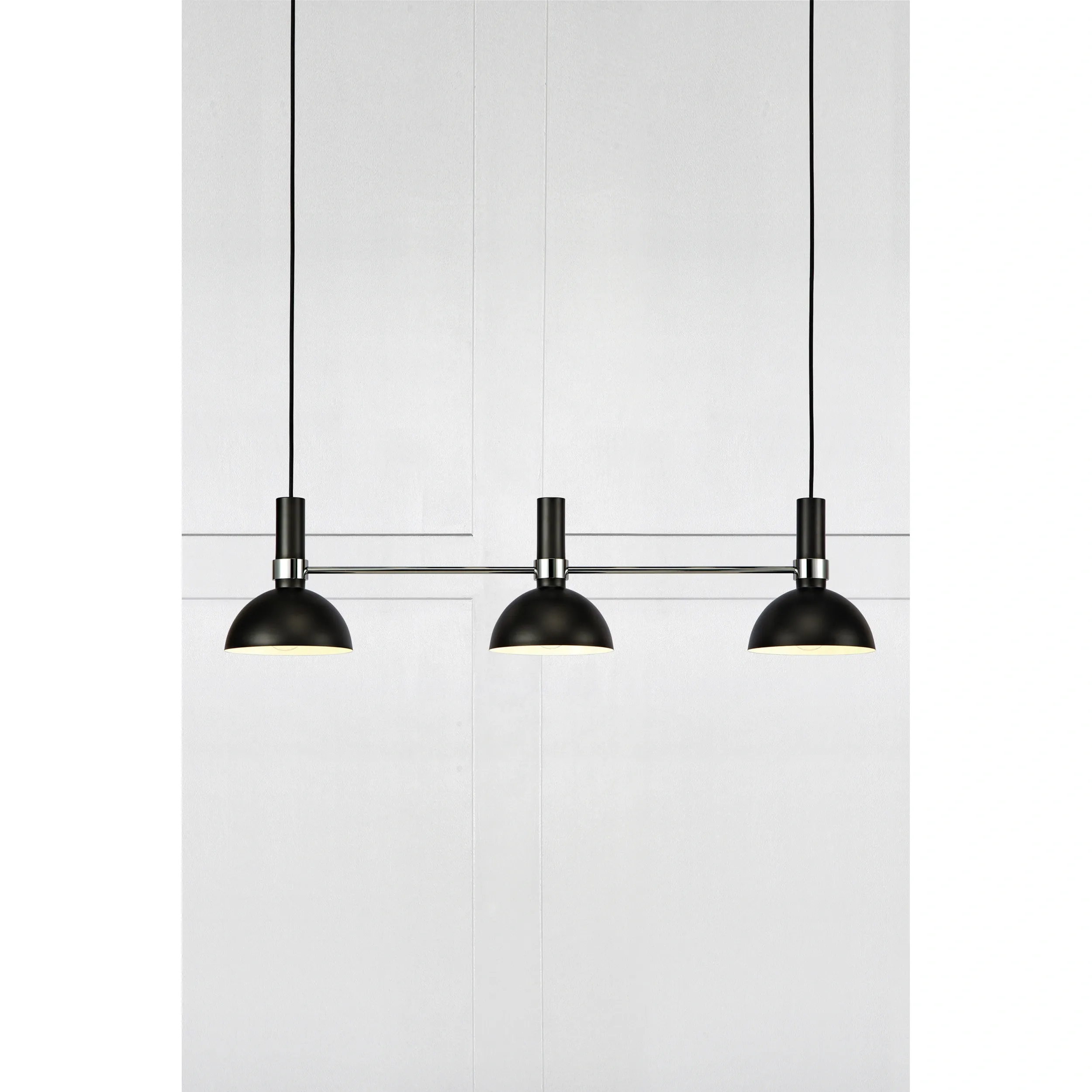 Lampa wisząca 3-punktowa w kolorze czarnym z metalowymi kloszami o zaokrąglonym kształcie, zawieszona na cienkich linkach. Klosze umieszczone na prostokątnej podstawie, w prostym, nowoczesnym stylu. Tło w jasnym kolorze.