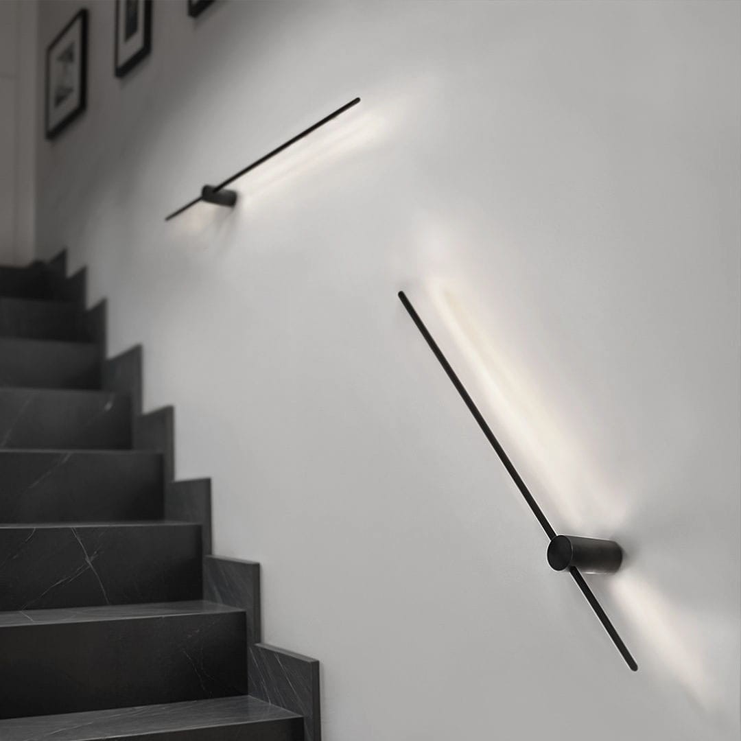 Kinkiet Uno 90 w kolorze czarnym, z jedną diodą LED o mocy 13W i temperaturze barwowej 4000K, zamontowany na ścianie wzdłuż schodów. Lampa ma minimalistyczny design z prostymi liniami, emitującym subtelne światło.