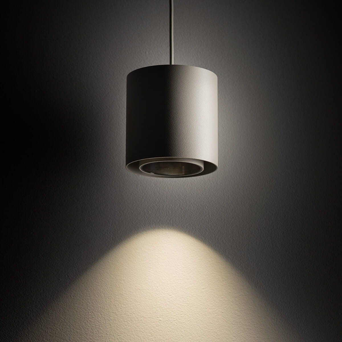 Lampa wisząca Point Duo w kolorze szarym z czarnymi akcentami, w kształcie cylindrycznym, zawieszona na cienkim przewodzie. Emituje skupione światło, tworząc efektowne oświetlenie na ścianie. Idealna do nowoczesnych wnętrz.