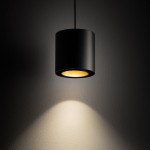 Lampa wisząca Point Duo w kolorze czarnym z złotym wnętrzem, o cylindrycznym kształcie. Zawieszona na cienkim kabelku, emituje ciepłe światło, które rzuca cień na ścianę. Idealna do nowoczesnych wnętrz.