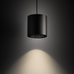 Czarna lampa wisząca Point Duo z oprawą na jedną żarówkę GU10, w kształcie cylindrycznym. Ujęcie z góry, z delikatnym światłem oświetlającym ścianę. Matowa powierzchnia, zawieszona na cienkim przewodzie. Tło w odcieniach szarości.