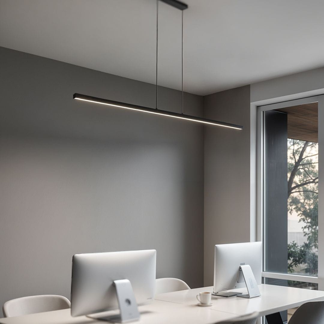 Lampa wisząca Linia 120, czarna, z jedną diodą LED 15W, w prostokątnym kształcie. Zawieszona nad biurkiem, z minimalistycznym designem, idealna do nowoczesnych wnętrz. Ujęcie z boku, w jasnym pomieszczeniu z komputerami i filiżanką.