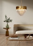 Lampa wisząca Lyon w złotym kolorze, z 9 miejscami na żarówki E14, o kształcie okrągłym z dekoracyjnym, plecionym kloszem. Zawieszona nad elegancką sofą w nowoczesnym wnętrzu, otoczona minimalistycznymi meblami i roślinnością.