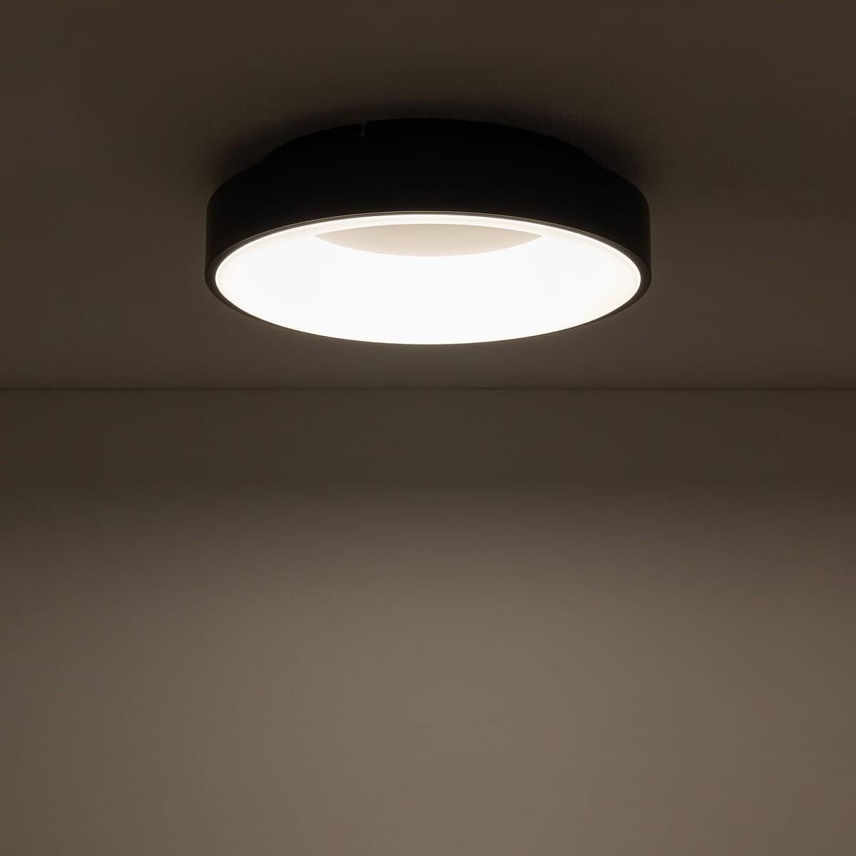 Plafon Nikki Round D38 w kolorze czarnym, o średnicy 38 cm, z jedną diodą LED 32W i temperaturze barwowej 4000K. Montowany sufitowo, okrągły kształt, emitujący jasne, neutralne światło. Tło stonowane, jednolite.
