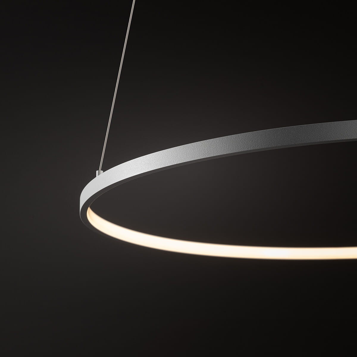 Lampa wisząca Circolo D60 w kolorze białym z okrągłym metalowym korpusem, zawieszona na cienkich żyłkach. Emituje ciepłe światło LED o mocy 21W i temperaturze 3000K, widoczna jest tylko górna część lampy. Tło ciemne, podkreślające design.