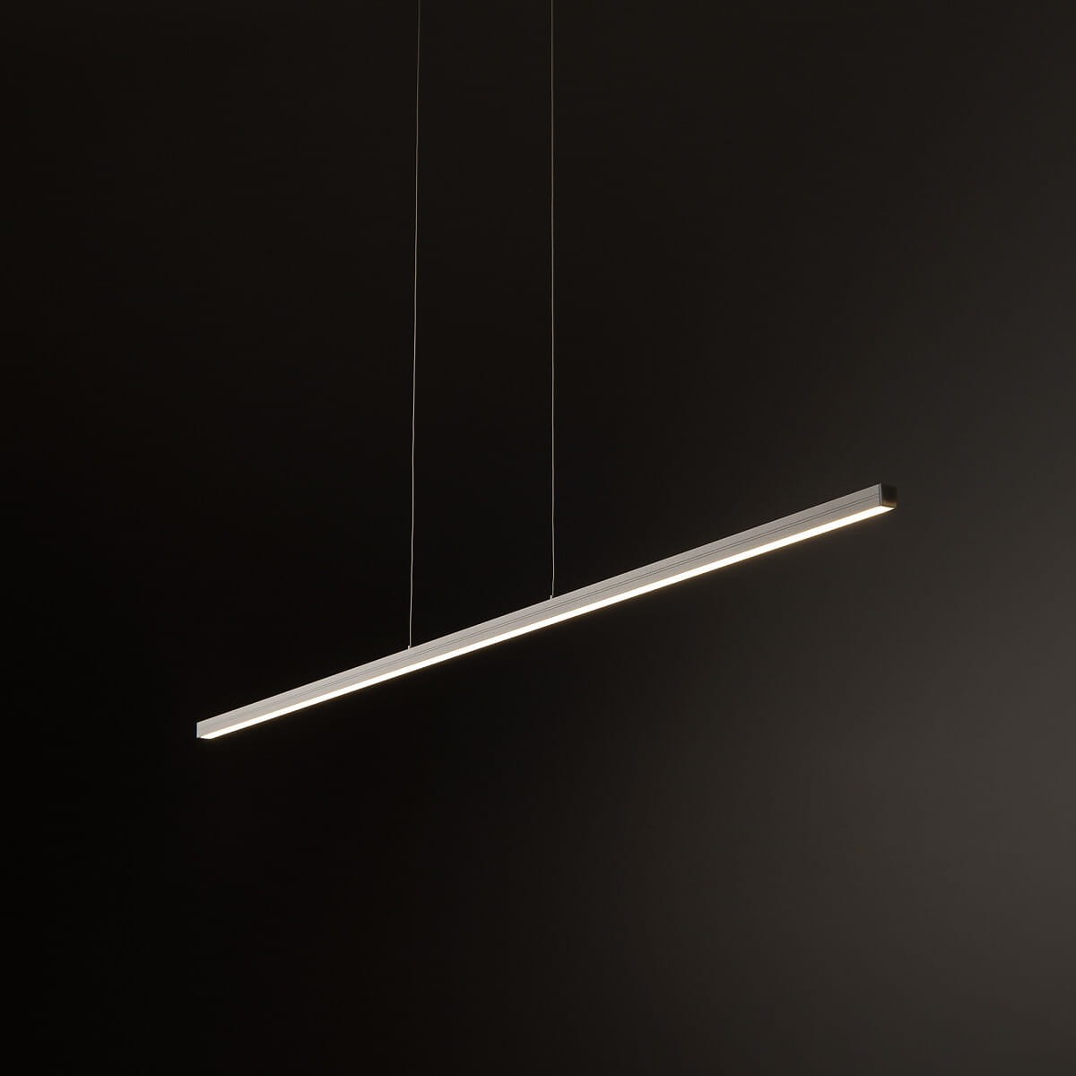 Lampa wisząca Bar L120, w kolorze białym, o prostokątnym kształcie. Wyposażona w jedno źródło światła LED o mocy 27W i temperaturze barwowej 3000K. Zawieszona na cienkich linkach, na ciemnym tle.