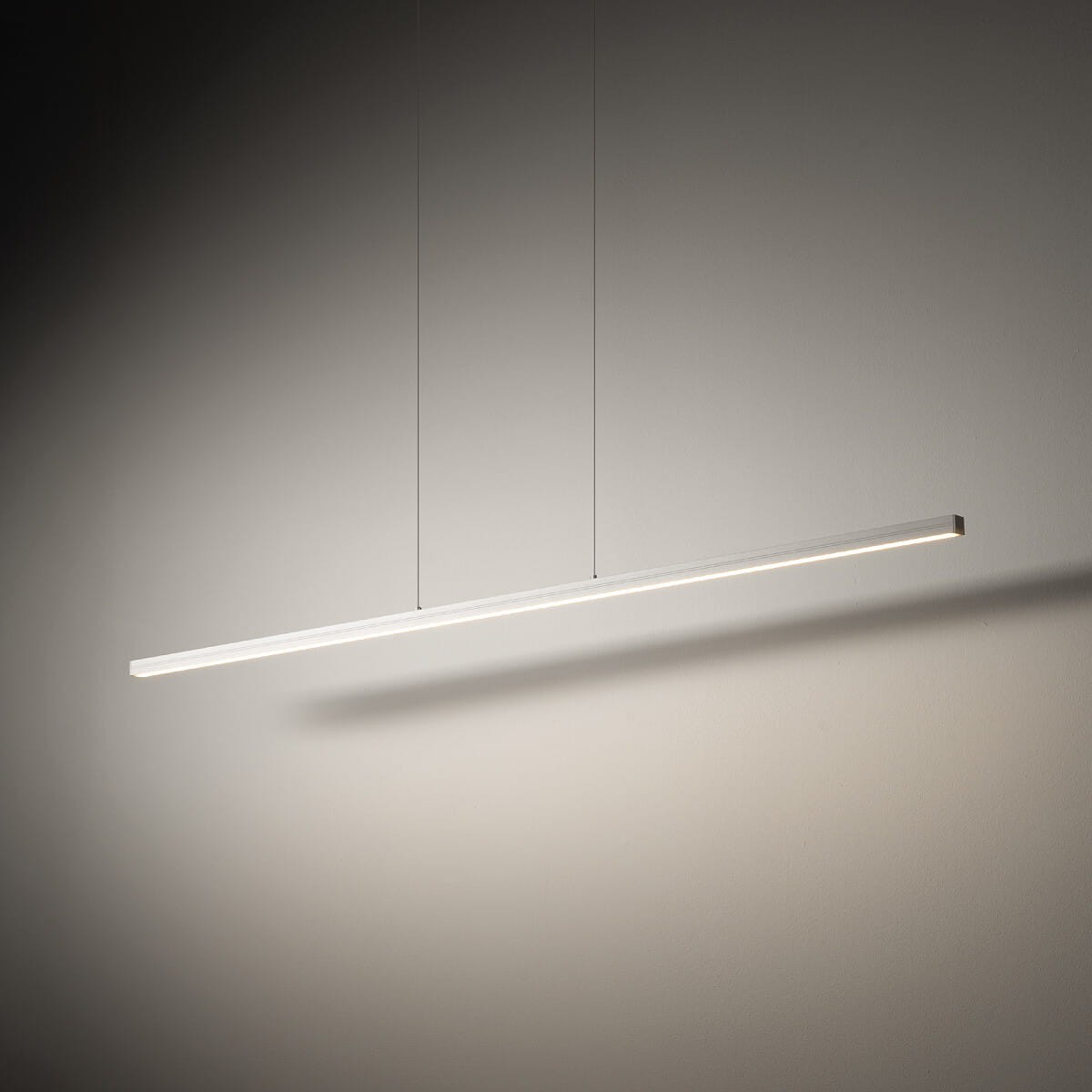 Lampa wisząca Bar L120 z białym korpusem, długości 120 cm, z jednolitą, cienką konstrukcją. Źródło światła LED, moc 27W, temperatura barwowa 4000K. Zawieszona na dwóch cienkich linkach, rzucająca delikatny cień na ścianę.
