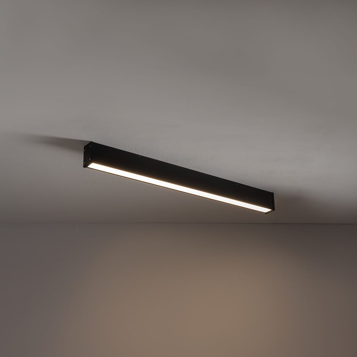 Czarna lampa sufitowa Outline LED S z jedną diodą LED, moc 35W, temperatura barwowa 3000K. Ujęcie frontalne, zamontowana pod sufitem, prostokątny kształt z wbudowanym źródłem światła. Tło w odcieniu szaro-beżowym.