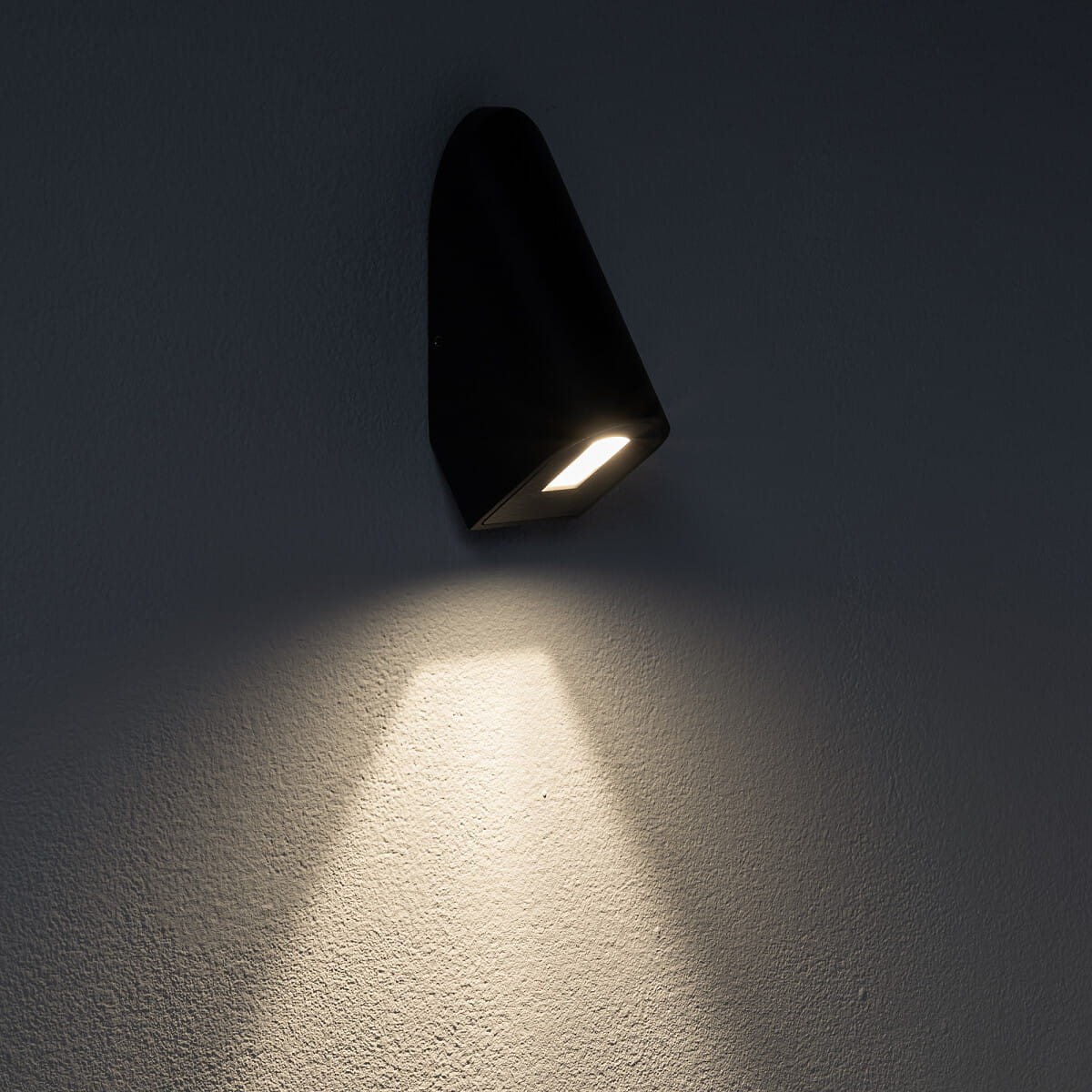 Kinkiet elewacyjny Cline w kolorze czarnym, z zamontowanym źródłem światła LED (1x3W, 3000K). Produkt o opływowym kształcie, montowany na ścianie, emitujący światło w dół na teksturowaną powierzchnię.