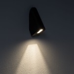 Kinkiet elewacyjny Cline w kolorze czarnym, z zamontowanym źródłem światła LED (1x3W, 3000K). Produkt o opływowym kształcie, montowany na ścianie, emitujący światło w dół na teksturowaną powierzchnię.