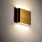 Kinkiet elewacyjny Semi S w kolorze mosiądzu, mocowany do ściany, emitujący ciepłe światło (3000K) z dwóch źródeł LED o mocy 6W. Kształt prostokątny z zaokrąglonymi krawędziami, podkreślający teksturę ściany.