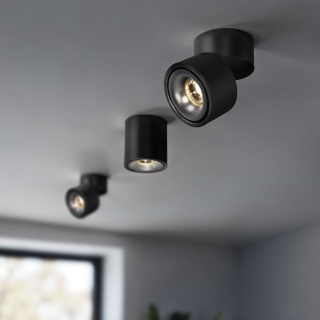 Czarna lampa sufitowa Tubo z trzema spotami LED, każdy o mocy 12W i barwie 3000K. Ujęcie z boku pokazuje lampę zamontowaną na suficie, z widocznymi oprawami lamp w cylindrycznym kształcie, emitującymi ciepłe światło.