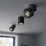 Czarna lampa sufitowa typu spot, LED o mocy 12W i temperaturze barwowej 4000K. Widoczna z boku, z trzema okrągłymi oprawami zamocowanymi do sufitu, emitującymi jasne światło. Tło jest jasne, z oknem w tle.