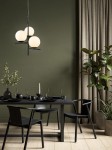 Lampa wisząca Pure w czarnym kolorze z trzema okrągłymi kloszami w jasnym odcieniu. Produkt zawieszony nad stołem w jadalni, otoczony ciemnymi krzesłami i dekoracjami, na tle zielonej ściany i zasłon.