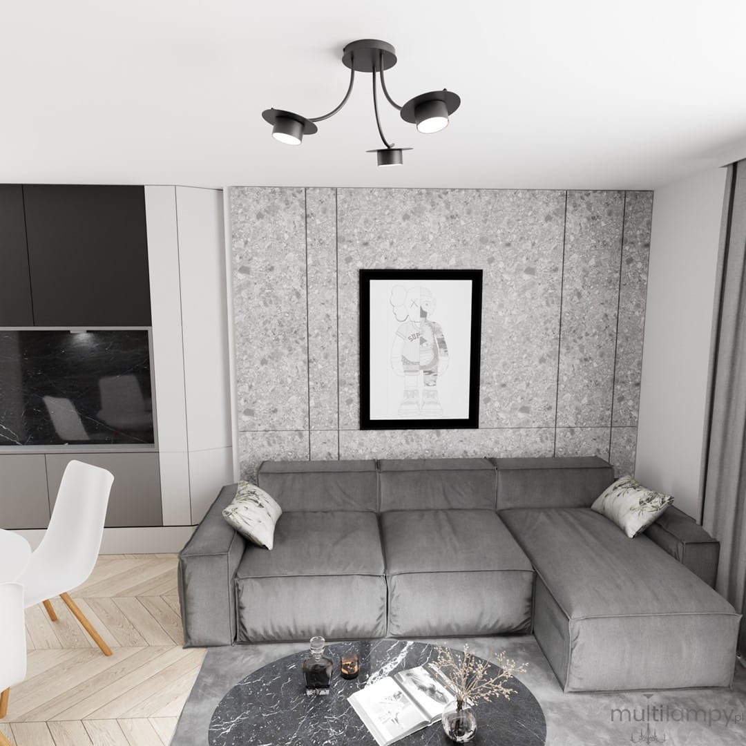 Lampa sufitowa Enso 3xGX53 w kolorze czarnym z trzema regulowanymi kloszami, zamontowana na suficie, w nowoczesnym wnętrzu z szarym narożnikiem i okrągłym stolikiem. Tło z teksturą betonu, z widocznym obrazem w ramie.