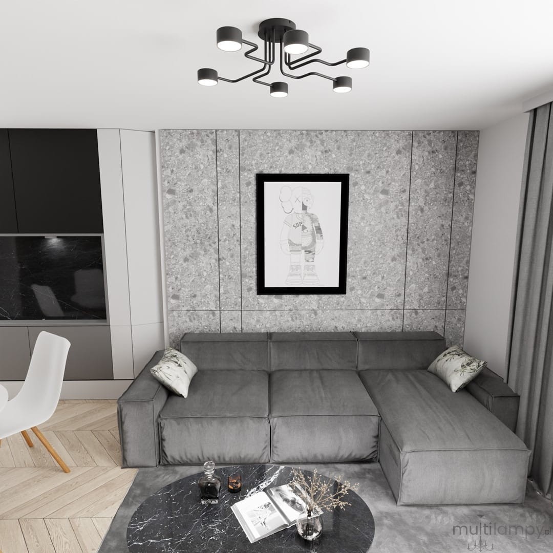 Lampa sufitowa Kurage w kolorze czarnym, z sześcioma źródłami światła GX53. Posiada nowoczesny, minimalistyczny kształt z wygiętymi ramionami, zamontowana na białym suficie, nad szaro-beżową kanapą w stylowym wnętrzu.
