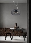 Lampa wisząca Valente w kolorze antracytowym z trzema oprawkami E27, z przezroczystym kloszem, zawieszona na cienkich linkach. W tle drewniane meble i stół, tworzące nowoczesną aranżację wnętrza.