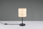 Lampa stołowa Aimee z czarną podstawą i naturalnym, teksturowanym kloszem z plecionki. Ujęcie frontalne, lampa stoi na białym stole, z widocznym kablem z włącznikiem. Tło w kolorze szarym.
